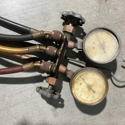 Sale Photo Thumbnail #16: Vintage HVAC manifold gauge set with brass fittings, dual pressure gauges, and attached hoses, showing signs of heavy use and age.