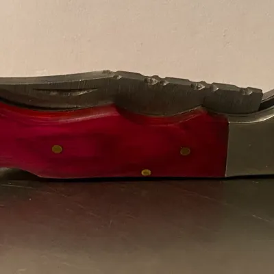 Sale Photo Thumbnail #70: Folding pocket knife featuring a vibrant pinkish-red handle with brass pins and a textured metal bolster.