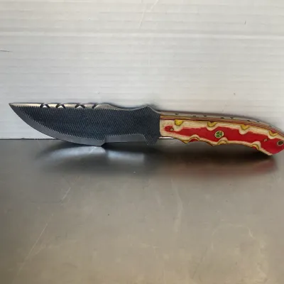 Sale Photo Thumbnail #59: Custom handmade knife crafted from a metal file, featuring a textured blade with a notched spine and a laminated wood handle in red, yellow, and natural tones.
