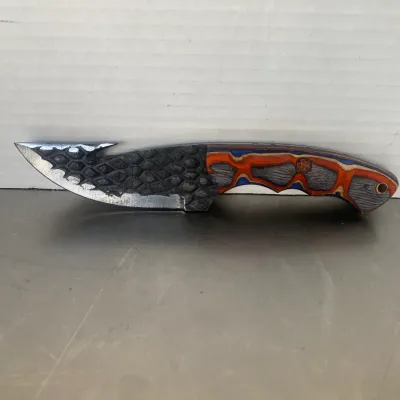 Sale Photo Thumbnail #21: Custom fixed-blade knife featuring a textured, scale-patterned blade with a gut hook and a colorful laminated wood handle in orange, blue, and grey tones.