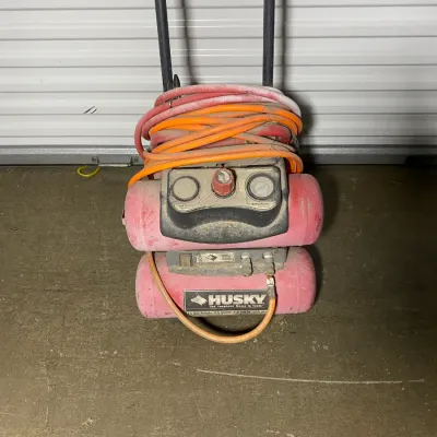 Sale Photo Thumbnail #4: Husky portable twin-stack air compressor with attached orange and red hoses, showing moderate dust and wear from use.