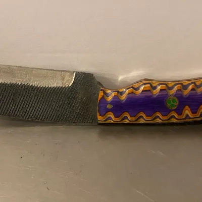 Sale Photo Thumbnail #76: Custom handmade knife crafted from a metal file, featuring a colorful purple, orange, and yellow laminated wood handle with a mosaic pin.