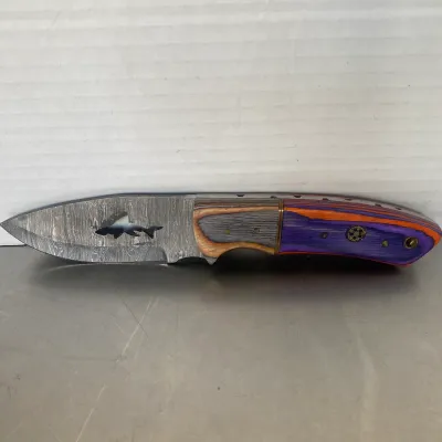 Sale Photo Thumbnail #57: Custom fixed-blade knife featuring a Damascus steel blade with a shark cutout and a colorful laminated wood handle in purple, orange, and natural tones.