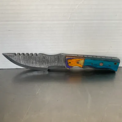 Sale Photo Thumbnail #24: Custom fixed-blade knife featuring a Damascus steel blade with a serrated spine and a colorful, multi-toned wooden handle.