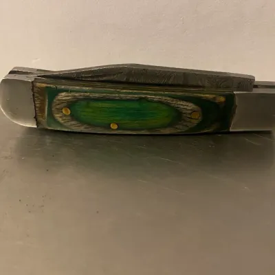 Sale Photo Thumbnail #73: Vintage folding pocket knife featuring a green and brown laminated wood handle with brass pins and stainless steel bolsters.