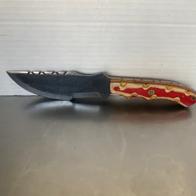 Sale Photo Thumbnail #25: Custom handmade knife crafted from a metal file, featuring a textured blade with a notched spine and a colorful laminated wood handle in red, yellow, and natural tones.