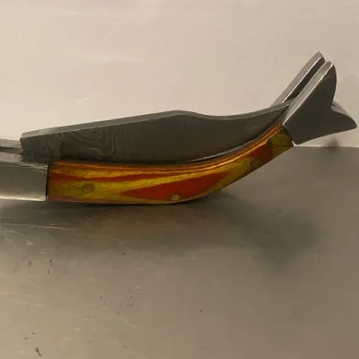 Sale Photo Thumbnail #74: Novelty fish-shaped folding pocket knife featuring a Damascus steel blade and a vibrant yellow and orange composite handle.
