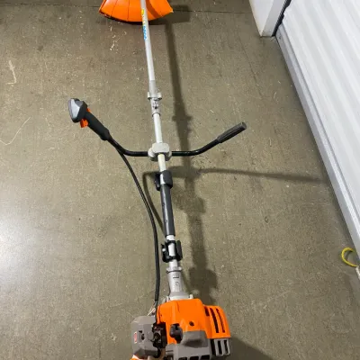 Sale Photo Thumbnail #11: Stihl gas-powered brushcutter with bike handles and orange safety guard, showing light wear from use.