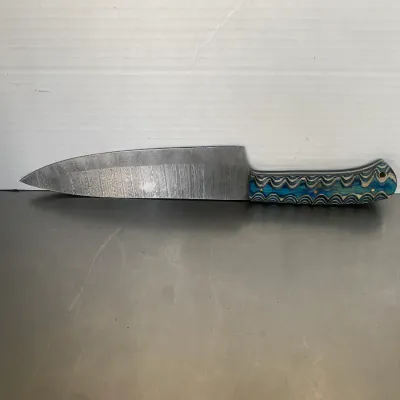 Sale Photo Thumbnail #44: Custom chef's knife featuring a Damascus steel blade and a vibrant blue and grey layered Micarta handle.