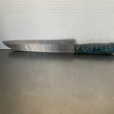 Sale Photo Thumbnail #37: Handcrafted chef's knife featuring a Damascus steel blade and a textured, multi-colored blue and green composite handle.