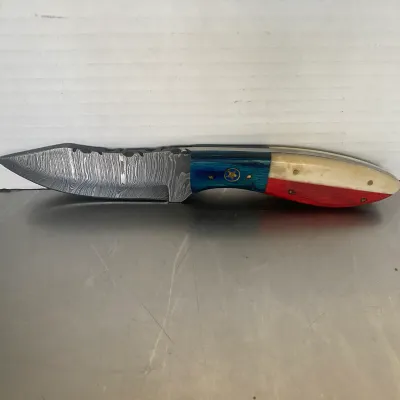 Sale Photo Thumbnail #66: Custom fixed-blade knife featuring a Damascus steel blade and a Texas flag-themed handle with blue, white, and red scales and a star emblem.