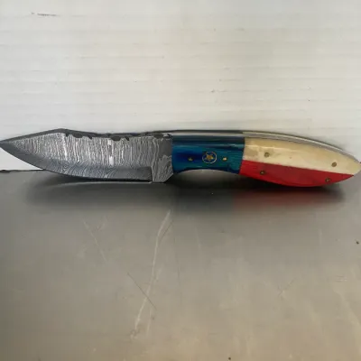 Sale Photo Thumbnail #32: Custom fixed-blade knife featuring a Damascus steel blade and a Texas flag-themed handle with blue, white, and red scales and a star emblem.