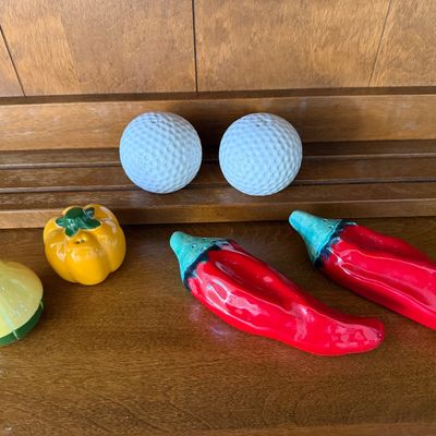 Sale Photo Thumbnail #155: A collection of three novelty ceramic salt and pepper shaker sets. Includes a pair of white golf balls, a pair of red chili peppers, and a yellow squash and orange bell pepper set. All pieces feature a glossy glazed finish. In good used condition with no 