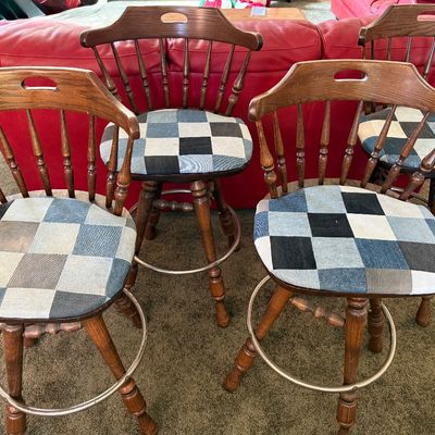 Sale Photo Thumbnail #247: A set of four vintage wooden swivel bar stools featuring a classic spindle back design and a circular metal footrest. The seats have been upholstered in a unique blue and grey denim patchwork fabric. The stools show some light wear on the wooden legs and 