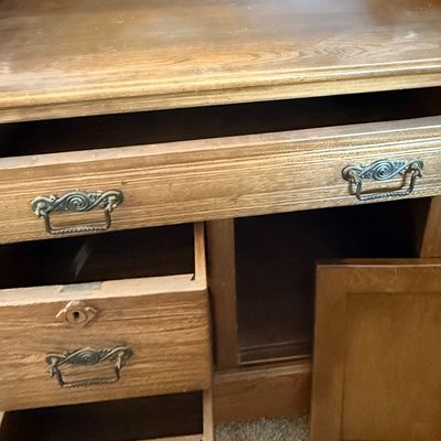 Sale Photo Thumbnail #170: An antique wooden washstand cabinet featuring a top gallery splashback, one wide top drawer, two smaller side drawers with keyholes, and a single cabinet door. The drawers showcase classic dovetail construction and are fitted with ornate metal pull handle
