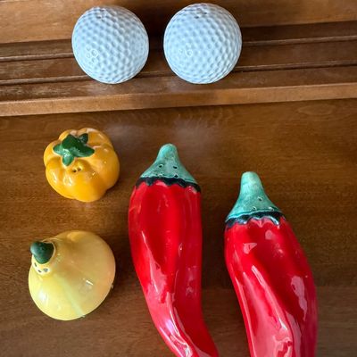 Sale Photo Thumbnail #156: A collection of three novelty ceramic salt and pepper shaker sets. Includes a pair of white golf balls, a pair of red chili peppers, and a yellow squash and orange bell pepper set. All pieces feature a glossy glazed finish. In good used condition with no 