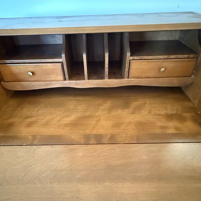 Sale Photo Thumbnail #162: A vintage wooden slant-front secretary desk featuring a drop-down writing surface that opens to reveal an interior organizer with small drawers and mail slots. The lower section includes three large drawers and a row of four smaller drawers, all accented 
