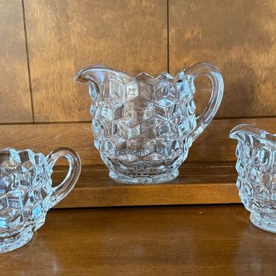 Sale Photo Thumbnail #133: A 3-piece set of vintage clear pressed glass tableware in the classic 'American' pattern by Fostoria (or similar cube/geometric design). The set includes a small pitcher/creamer measuring approximately 4.5 inches tall, a smaller creamer, and a double-hand