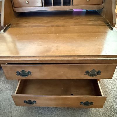 Sale Photo Thumbnail #163: A vintage wooden slant-front secretary desk featuring a drop-down writing surface that opens to reveal an interior organizer with small drawers and mail slots. The lower section includes three large drawers and a row of four smaller drawers, all accented 