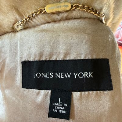 Sale Photo Thumbnail #269: A stylish Jones New York faux fur coat in a warm honey-blonde/tan color. Features a textured, ruffled collar, tiered panel design, and a smooth satin-like lining. Includes a gold-tone chain hanging loop. Size Large (L). Made in China. Appears to be in ver