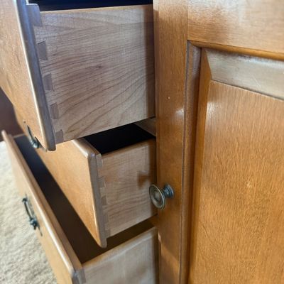 Sale Photo Thumbnail #10: A vintage two-piece wooden hutch featuring a top cabinet with louvered doors, open shelving, and plate grooves, sitting on a base with three central dovetail drawers, two side cabinets, and two wide bottom drawers. Features classic brass-toned hardware. P