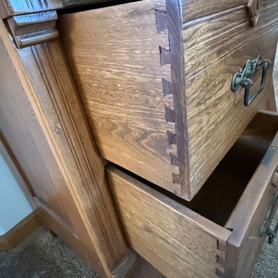 Sale Photo Thumbnail #171: An antique wooden washstand cabinet featuring a top gallery splashback, one wide top drawer, two smaller side drawers with keyholes, and a single cabinet door. The drawers showcase classic dovetail construction and are fitted with ornate metal pull handle