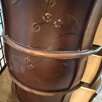 Sale Photo Thumbnail #178: A charming round wooden accent chest or nightstand featuring three curved drawers. The drawer fronts are finished in a deep burgundy/mauve tone and hand-painted with delicate bird and floral branch motifs. Features metal ring pull hardware. Shows some lig