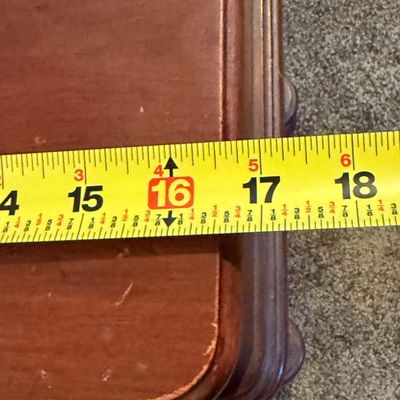 Sale Photo Thumbnail #85: A vintage wooden side table featuring a decorative lyre-shaped base, a single drawer with a carved leaf pull, and turned drop finials. The table top shows some light surface wear and minor scuffs consistent with age and use. Measures approximately 16.5 in