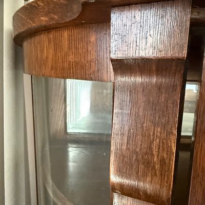 Sale Photo Thumbnail #188: An antique tiger oak china display cabinet featuring a curved glass front door and curved glass side panels. The cabinet includes five wooden shelves, a mirrored upper back section, and elegant carved wood details. It is fitted with a vintage brass and fa