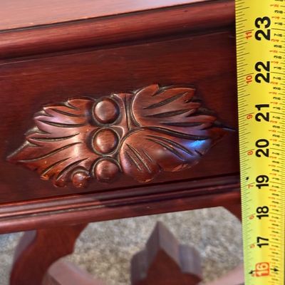 Sale Photo Thumbnail #87: A vintage wooden side table featuring a decorative lyre-shaped base, a single drawer with a carved leaf pull, and turned drop finials. The table top shows some light surface wear and minor scuffs consistent with age and use. Measures approximately 16.5 in
