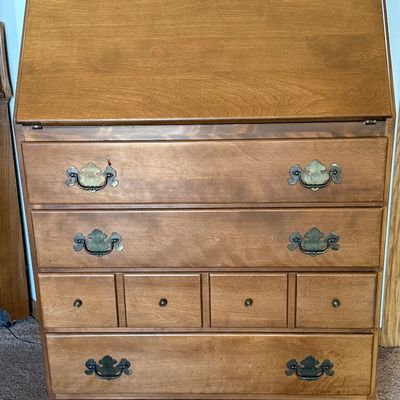 Sale Photo Thumbnail #160: A vintage wooden slant-front secretary desk featuring a drop-down writing surface that opens to reveal an interior organizer with small drawers and mail slots. The lower section includes three large drawers and a row of four smaller drawers, all accented 