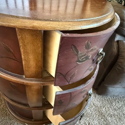 Sale Photo Thumbnail #177: A charming round wooden accent chest or nightstand featuring three curved drawers. The drawer fronts are finished in a deep burgundy/mauve tone and hand-painted with delicate bird and floral branch motifs. Features metal ring pull hardware. Shows some lig