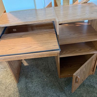 Sale Photo Thumbnail #233: A vintage-style laminate wood computer desk featuring an oak grain finish. Designed with a slide-out keyboard tray on metal tracks, open shelving compartments, and a lower storage cabinet with a single door. Ideal for small spaces, home offices, or studen