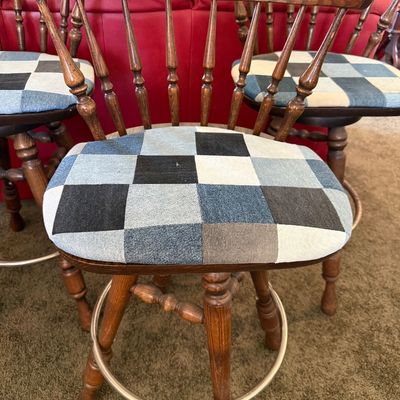 Sale Photo Thumbnail #248: A set of four vintage wooden swivel bar stools featuring a classic spindle back design and a circular metal footrest. The seats have been upholstered in a unique blue and grey denim patchwork fabric. The stools show some light wear on the wooden legs and 