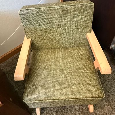 Sale Photo Thumbnail #242: A vintage child-sized armchair featuring a mid-century modern aesthetic. It is upholstered in a textured green woven fabric with light-colored wooden armrests and legs. The chair shows some signs of wear, including light scuffs and scratches on the wooden