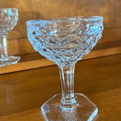 Sale Photo Thumbnail #119: A set of four vintage clear pressed glass champagne coupe or sherbet glasses. Features a textured diamond/honeycomb pattern on the bowl, a faceted stem, and a hexagonal base. Each glass measures approximately 4.5 inches tall. All pieces appear to be in go