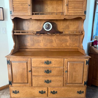 Sale Photo Thumbnail #12: A vintage two-piece wooden hutch featuring a top cabinet with louvered doors, open shelving, and plate grooves, sitting on a base with three central dovetail drawers, two side cabinets, and two wide bottom drawers. Features classic brass-toned hardware. P
