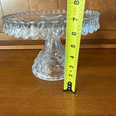 Sale Photo Thumbnail #49: A vintage clear pressed glass pedestal cake stand featuring the classic Fostoria 'American' 3D cube pattern. Features a scalloped, draped rim and a textured, flared pedestal base. Excellent condition with no visible chips, cracks, or clouding. Measures ap