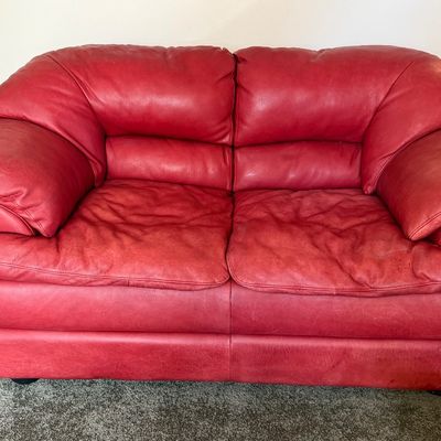 Sale Photo Thumbnail #94: A vibrant red leather loveseat by Natuzzi. Features plush, overstuffed armrests and back cushions. Shows some light wear and creasing consistent with gentle use, but remains in good, comfortable condition. Includes original Natuzzi documentation. Measures