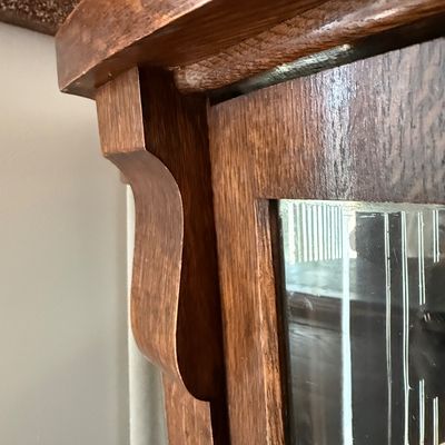 Sale Photo Thumbnail #193: An antique tiger oak china display cabinet featuring a curved glass front door and curved glass side panels. The cabinet includes five wooden shelves, a mirrored upper back section, and elegant carved wood details. It is fitted with a vintage brass and fa