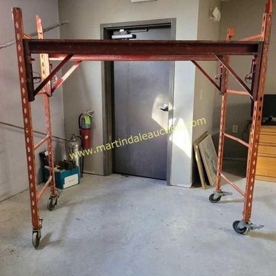 Sale Photo Thumbnail #50: Heavy-duty rolling scaffolding unit with an orange metal frame and locking casters, showing some wear from use.