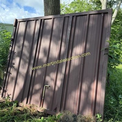 Sale Photo Thumbnail #49: Large brown corrugated metal gate or panel with a heavy-duty frame, leaning against a tree in an outdoor grassy area.