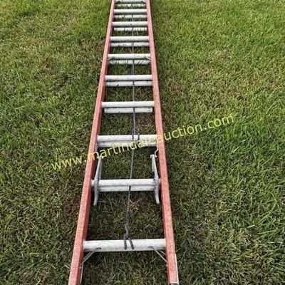 Sale Photo Thumbnail #15: 32ft fiberglass extension ladder with orange rails and aluminum rungs, showing some wear from outdoor use.