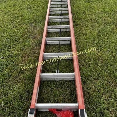 Sale Photo Thumbnail #14: 32ft Orange fiberglass extension ladder with aluminum rungs, showing some wear from outdoor use.