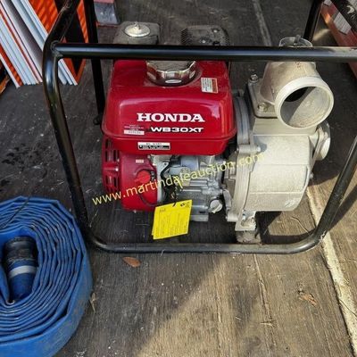 Sale Photo Thumbnail #23: Honda WB30XT 3-inch water pump with a red engine housing and black protective frame, accompanied by a coiled blue discharge hose.