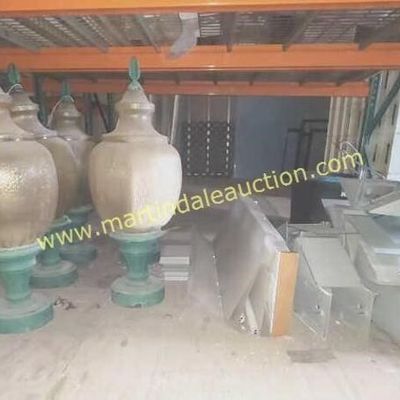 Sale Photo Thumbnail #44: Collection of large vintage outdoor post-mount light globes with textured gold-tone bodies and green painted bases, stored alongside metal brackets in a warehouse setting.
