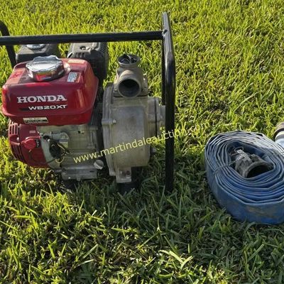Sale Photo Thumbnail #22: Honda WB20XT portable water pump with protective roll cage frame, shown alongside a coiled blue discharge hose on a grassy lawn.
