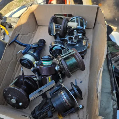 Sale Photo Thumbnail #11: Assorted vintage fishing reels, including spinning and conventional models, displayed in a cardboard box.