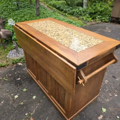 Sale Photo Thumbnail #50: Mission-style oak kitchen island or bar cart featuring a granite-inlaid top, a drop-leaf extension, and a wooden towel bar on the side. 48 wideX24 deepX36 high with 12 in drop leaf