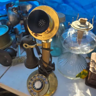 Sale Photo Thumbnail #27: Vintage brass candlestick telephone with a rotary dial, displayed alongside a clear glass oil lamp and other antique collectibles.